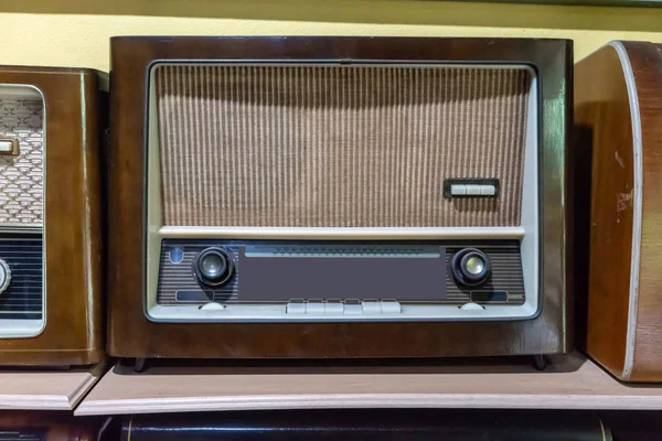 Retro broadcast radio receiver on wooden shelf against yellow wall background.