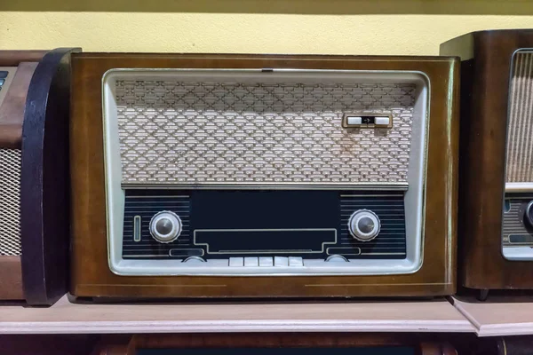 Retro broadcast radio receiver on wooden shelf against yellow wall background.