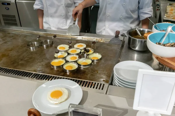 Hotel chef hands with gloves cooking fried eggs  on hot pan