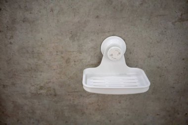 White plastic soap dish mounted the modern cement wall.  clipart