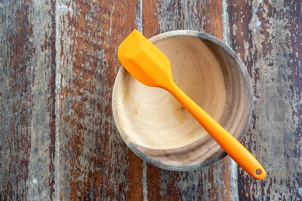 Orange silicone spatula with wooden bowl on wooden table