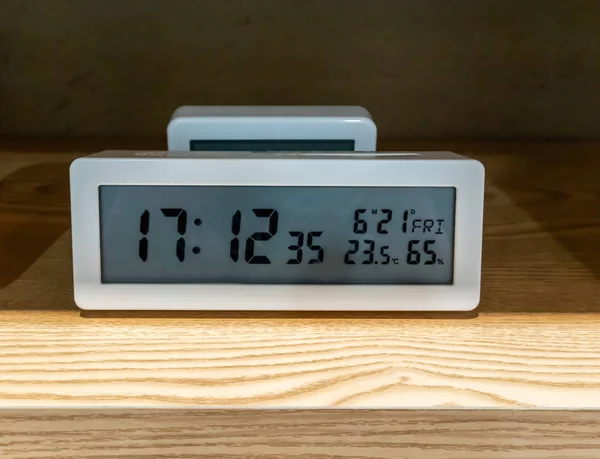White pocket digital clock on wooden shelf