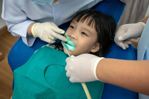 Asian girl biting silicon tray of Fluoride and dental suction.