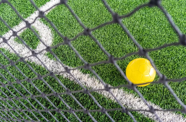 Uno sguardo attraverso la rete di calcio concentrandosi sulla palla gialla su un — Foto Stock