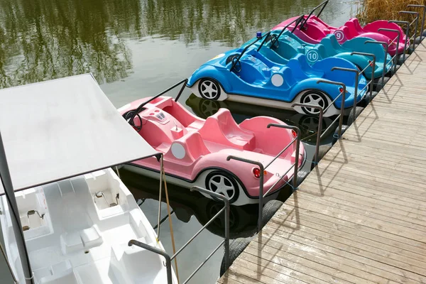 Catamarani auto colorate e catamarano bianco sul lago in parco. In piedi al molo . — Foto Stock