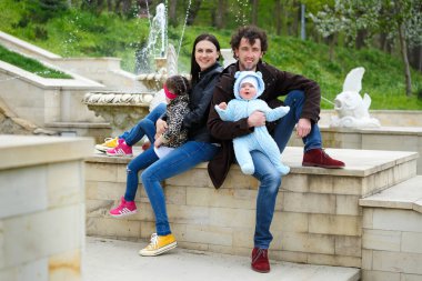 Aile hayatı. Babaların çocukları Çeşme arka plan üzerinde oturmak. Kız rahatsız ve uzaklaştı. Yatay olarak çerçeveli atış.