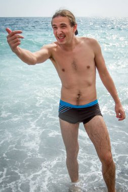 Genç bir adam deniz suyu ayakta ve birini aramak. Dikey olarak çerçeveli atış.