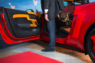 Bir adam bir şık takım elbise çıkmadan kırmızı supercar için kırmızı halı olay. Yatay olarak çerçeveli atış.