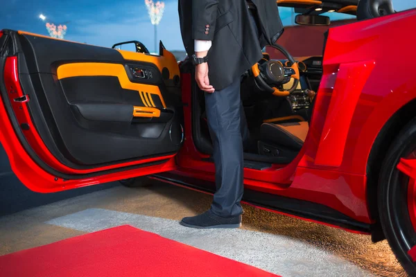 Bir adam bir şık takım elbise çıkmadan kırmızı supercar için kırmızı halı olay. Yatay olarak çerçeveli atış.