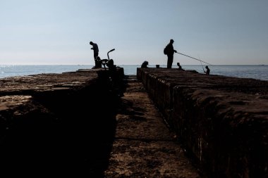 Balıkçılar iskelede Balık tutma. Dalgakıran insan etkileşimi. Siluet fotoğraf. Ön planda bir bisiklet olduğunu.