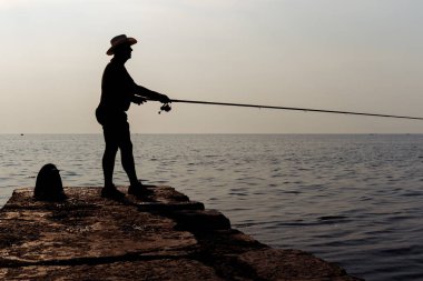 Bir iskelede şafak gökyüzü arka plan üzerinde duran balıkçı. Siluet fotoğraf.