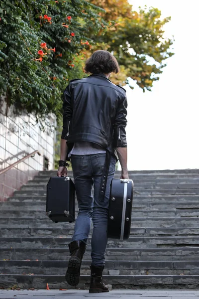 Street musician holding a case with a guitar and amplifier. It rises up the stairs of the underpass. Vagrant lifestyle. Playing to make money a living. Unemployed musician. Future rock star. Vertically framed shot.