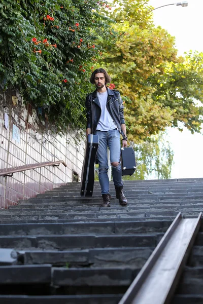 Street musician holding a case with a guitar and amplifier. Goes down the stairs to the underground passage. Vagrant lifestyle. Playing to make money a living. Unemployed musician. Future rock star. Vertically framed shot.