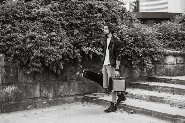 Street musician holding a case with a guitar and amplifier. Vagrant lifestyle. Playing to make money a living. Unemployed musician. Future rock star. Horizontally framed shot.