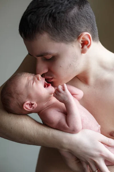 Ojciec posiada swojego nowonarodzonego syna w jego ręce. Chłopiec płacze, człowiek stara się go uspokoić. Życie rodzinne. Urodził się człowiek. — Zdjęcie stockowe