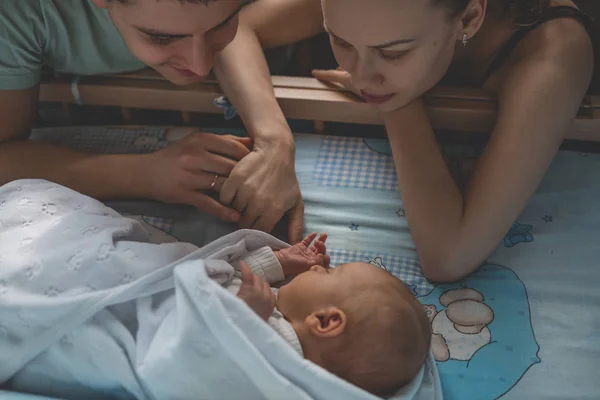Kadın ve erkek yeni doğmuş bebek bak. Çocuk onun beşiğinde uyuyor. Anne, baba ve bebek. Genç aile portresi. Mutlu aile hayatı. Adam doğdu.