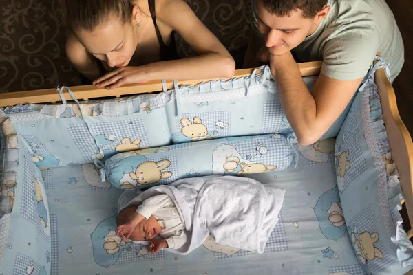 Kobieta i mężczyzna spojrzeć na noworodka. Chłopiec odgrywa w jego szopka. Mama, Tata i dziecko. Portret młodej rodziny. Szczęśliwe życie rodzinne. Urodził się człowiek. — Zdjęcie stockowe