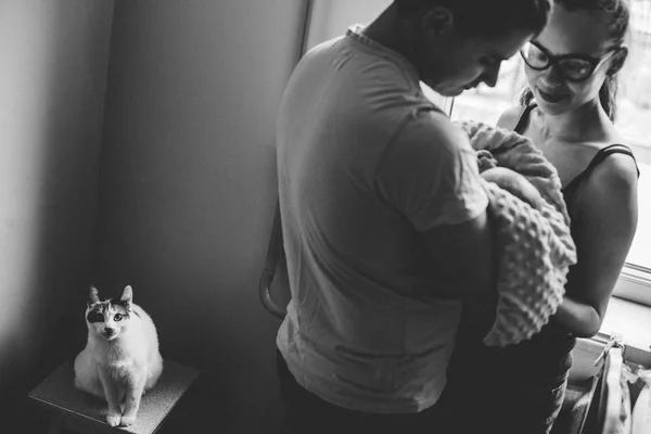 Rodzina scena. Kobieta i mężczyzna, trzymając w rękach noworodka. Obok nich na stołku siedzi kot. Szczęśliwe życie rodzinne. Urodził się człowiek. — Zdjęcie stockowe