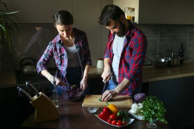 Güzel genç çift mutfakta yemek sağlıklı yemek sırasında evde. Koca salatalık keser. Karısı karışımı salata. Olay yerinden aile hayatı.