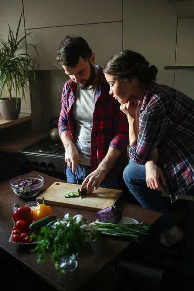 Güzel genç çift mutfakta yemek sağlıklı yemek sırasında evde. Kesim salata adamdır. Kadın tablo ve saatler üzerinde oturur. Olay yerinden aile hayatı. — Stok fotoğraf