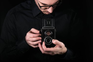 Fotoğraf makinesi tutan bir fotoğrafçı. Çekim süreci. Siyah arka planda Retro fotoğraf kamerası orta format ikiz lens refleks kamera.