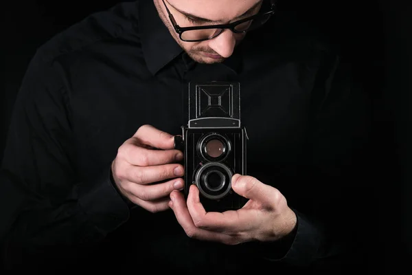 男子摄影师拿着相机。拍摄过程。复古照片相机中等格式双镜头反射相机在黑色背景. — 图库照片