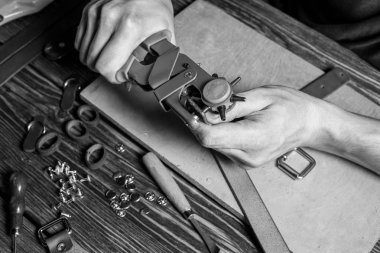 Bir delik yumruk ve deri parçası tutan usta. Araçları ve aksesuarları ile dağınık kahverengi ahşap masa.