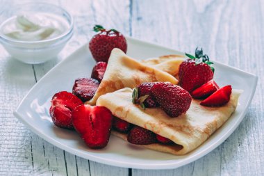 Çilek ile krep. Beyaz ahşap zemin üzerinde.