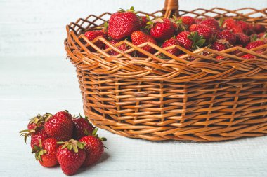 Hasır sepet ile olgun çilek dolu. Beyaz ahşap zemin üzerinde.