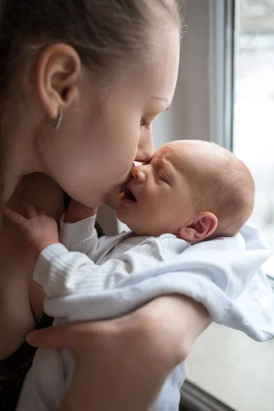 Nő a gazdaság, a kezében egy újszülött. Anya fia csók. Portré fiatal család. Boldog családi élet. Ember született. — Stock Fotó