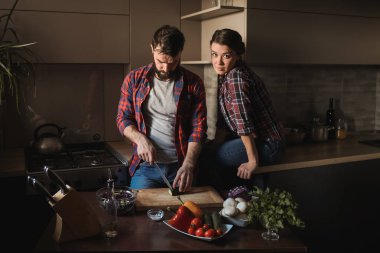 Güzel genç çift mutfakta yemek sağlıklı yemek sırasında evde. Kesim salata adamdır. Kadın masaya oturur ve çerçeve içinde görünüyor. Olay yerinden aile hayatı.