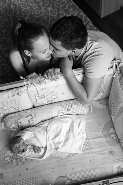 Man and a woman near their newborn. Parents kiss. Boy cries in his crib. Mom, dad and baby. Portrait of young family. Family life. Man was born. — Stock Photo, Image