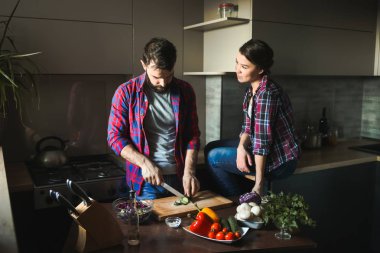Güzel genç çift mutfakta yemek sağlıklı yemek sırasında evde. Kesim salata adamdır. Kadın masaya oturur ve kocası görünüyor. Olay yerinden aile hayatı.