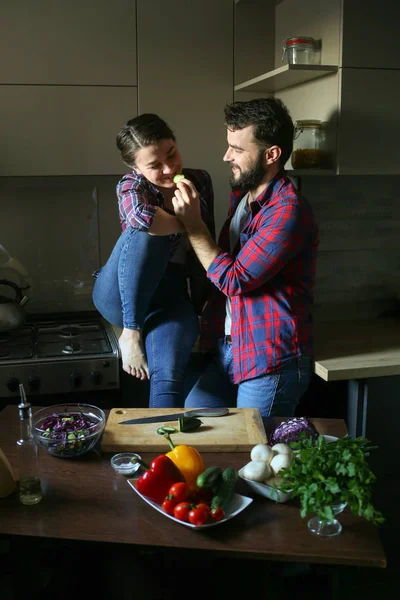 Güzel genç çift mutfakta yemek sağlıklı yemek sırasında evde. Koca salata keser ve eşi salatalık beslenir. Olay yerinden aile hayatı. — Stok fotoğraf