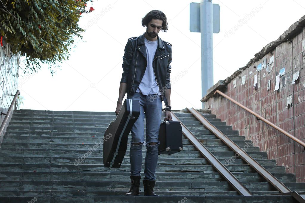 Street musician holding a case with a guitar and amplifier. Goes down the stairs to the underground passage. Vagrant lifestyle. Playing to make money a living. Unemployed musician. Future rock star.