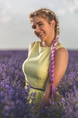 Uzun pembe örgüleri olan genç, güzel sarışın bir lavanta tarlasında duruyor..