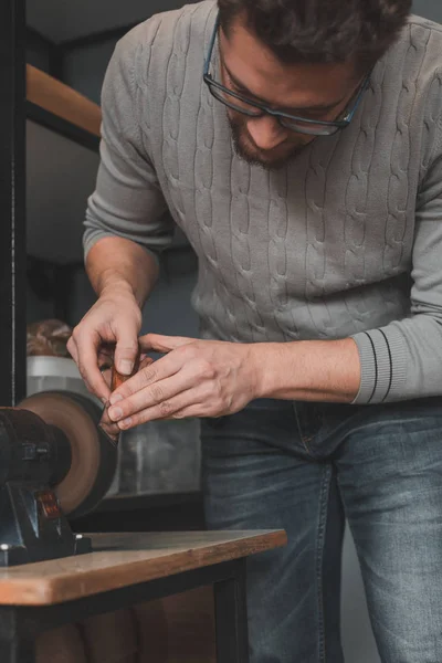 Kožený řemeslník zostří nůž na řezání kůže na brusku. Ručně vyrobený koncept. Koncepce malých podniků pro tvorbu kožených výrobků. — Stock fotografie