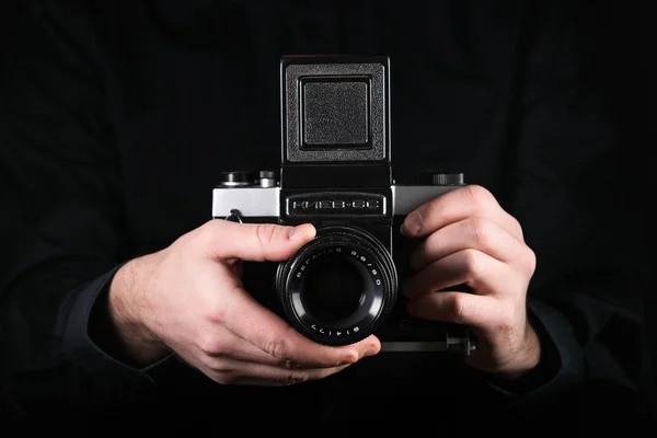 摩尔多瓦共和国基希讷乌 - 2019年3月12日：男子摄影师手持相机。拍摄过程。复古照片相机在黑色背景的中等格式。俄罗斯相机基辅 6c. — 图库照片