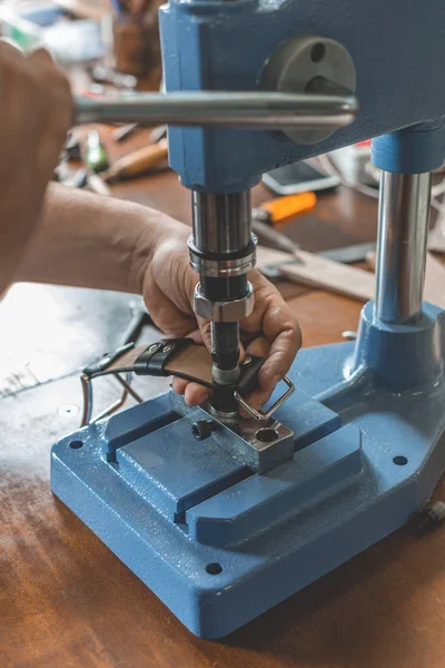 Maître travaille sur la presse avec la peau. Sur une table en bois marron parsemée d'outils et accessoires . — Photo