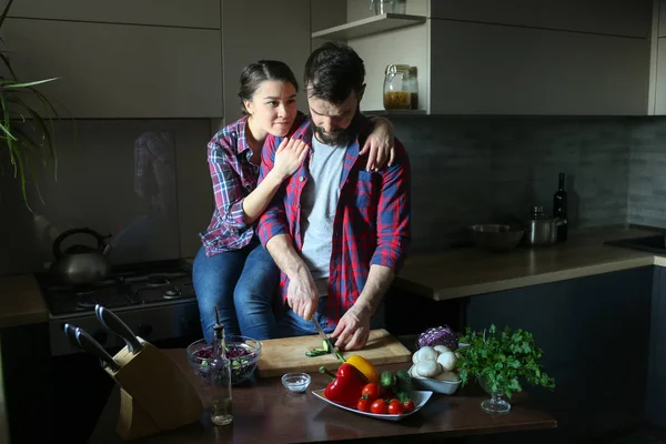 Güzel genç çift mutfakta yemek sağlıklı yemek sırasında evde. Kesim salata adamdır. Kadın masaya oturur ve adam arkadan sarılarak. Olay yerinden aile hayatı. — Stok fotoğraf