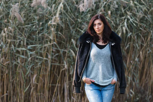 Beautiful brunette standing on a background of reeds. — Stock Photo, Image