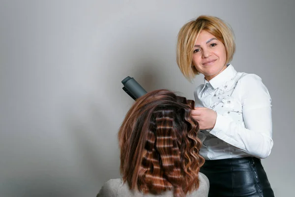Hair salon. Woman hairstyle. Hairdresser curls hair client.