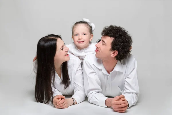 Portrait of a happy family. Parents are leaning on elbows and their daughter hugging them. On white background.