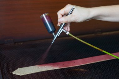 Deri ustası kayışlar üzerinde boya neden olur. Mor boyaile sprey tabancası. El yapımı konsept. Deri ürünleri oluşturmak için küçük işletme kavramı.