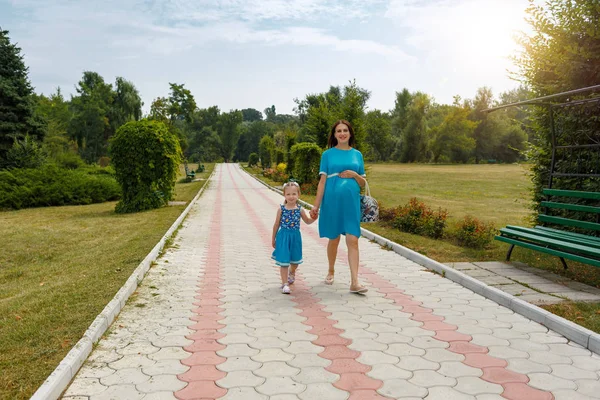 Вагітна жінка і дівчина тримає руки, ходячи в парку. Щаслива концепція сімейного життя. Яскравий сонячний день і багато зелених рослин . — стокове фото