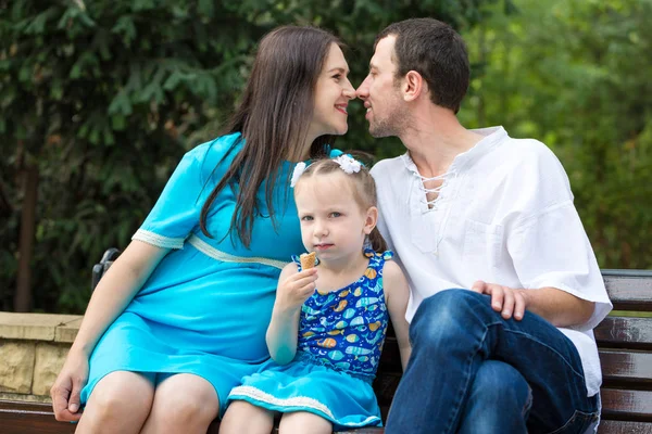 Parkta bir bankta oturan aile. Waffle bardağı yiyen küçük bir kız. Hamile bir kadın. Mutlu aile hayatı kavramı. — Stok fotoğraf