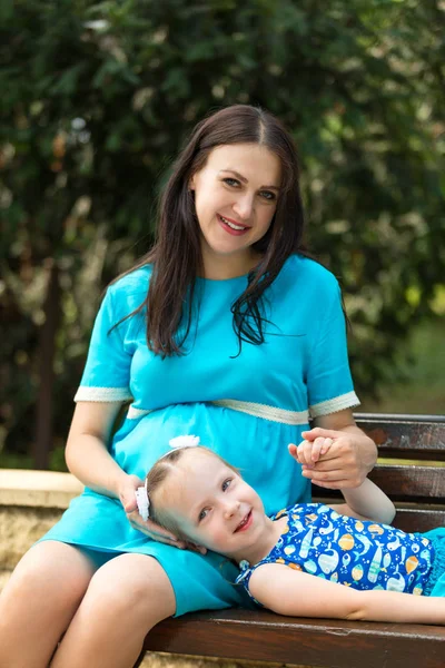 A pregnant woman and a girl resting on a bench. Happy family life concept. Royalty Free Stock Photos