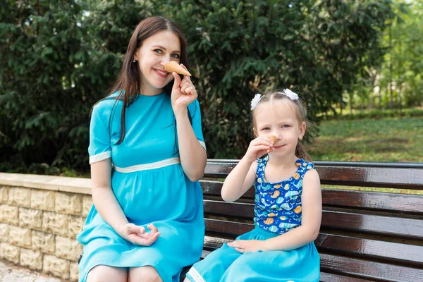 Mom and daughter sit on bench and play with waffle cups. They make a nose like Pinocchio\'s.