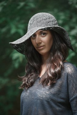 Yeşil yaprakların arka planda duran mavi elbise ve siyah şapka güzel bir kız portresi kadar kapatın. Güneş ışığı şapkayı kırAr ve yüzüne düşer..
