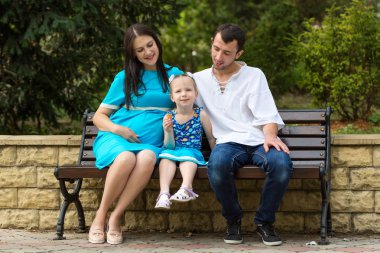 Parkta bir bankta oturan aile. Waffle bardağı yiyen küçük bir kız. Hamile bir kadın. Mutlu aile hayatı kavramı.